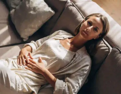 Frau liegt auf einer Couch und hält sich den Unterleib