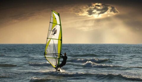 Windsurfer fährt auf dem Wasser Richtung Sonnenuntergang