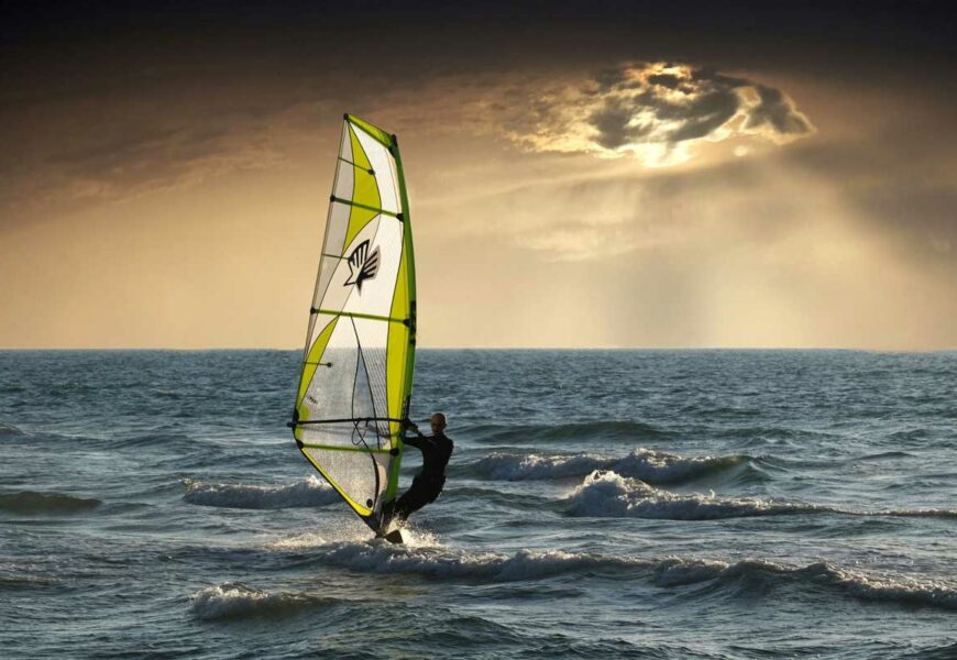 Windsurfer fährt auf dem Wasser Richtung Sonnenuntergang