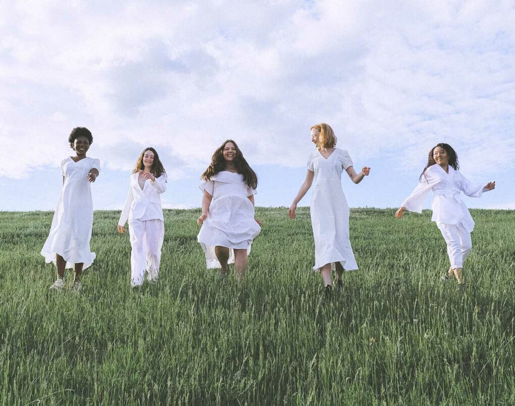 Frauen laufen gemeinsam mit weißen Klamotten über eine Wiese