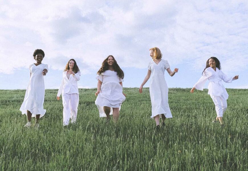 Frauen laufen gemeinsam mit weißen Klamotten über eine Wiese