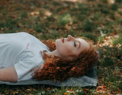 Frau liegt draußen auf einer Yogamatte im Shavasana mit geschlossenen Augen und macht Yoga