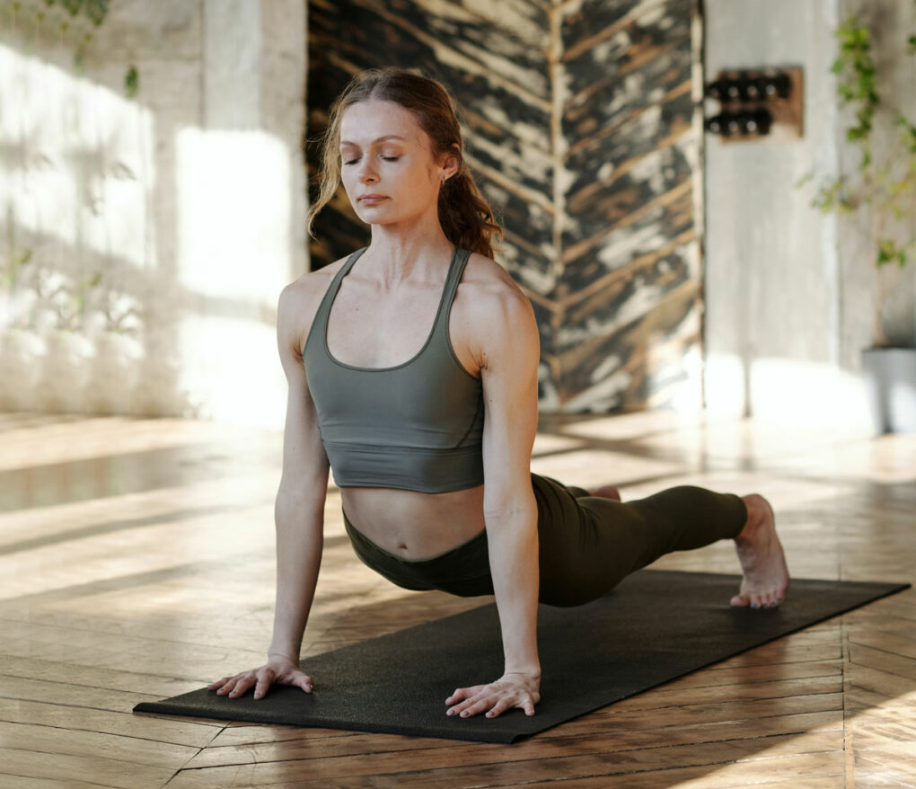 Frau hat die Augen geschlossen und macht Yoga auf einer Yogamatte in der Yogaübung Krähe