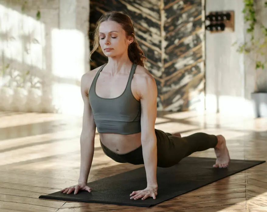 Frau hat die Augen geschlossen und macht Yoga auf einer Yogamatte in der Yogaübung Krähe