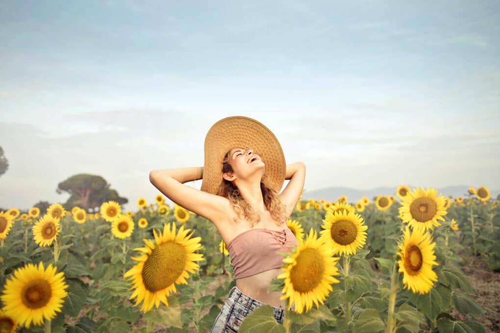Frau steht glücklich in einem Sonnenblumenfeld und lacht