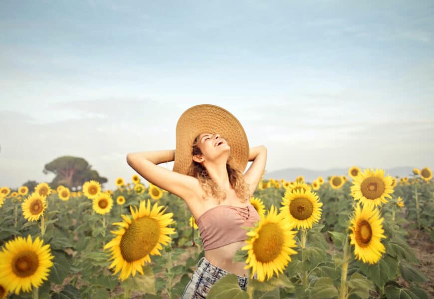 Frau steht glücklich in einem Sonnenblumenfeld und lacht