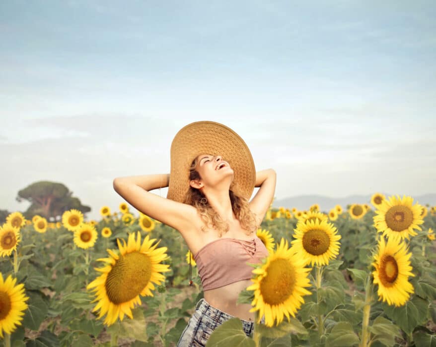 Frau steht glücklich in einem Sonnenblumenfeld und lacht