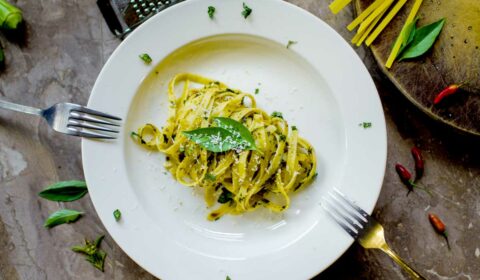 Ein weißer Teller mit Nudeln mit grünem Pesto und frischem Parmesan