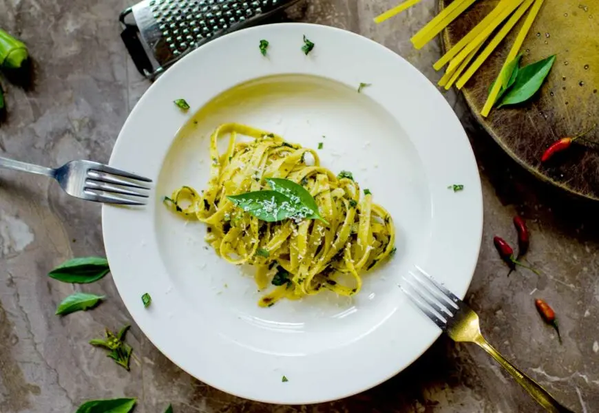 Ein weißer Teller mit Nudeln mit grünem Pesto und frischem Parmesan