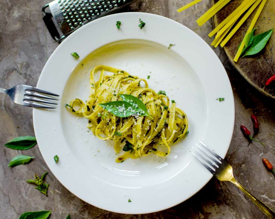 Ein weißer Teller mit Nudeln mit grünem Pesto und frischem Parmesan
