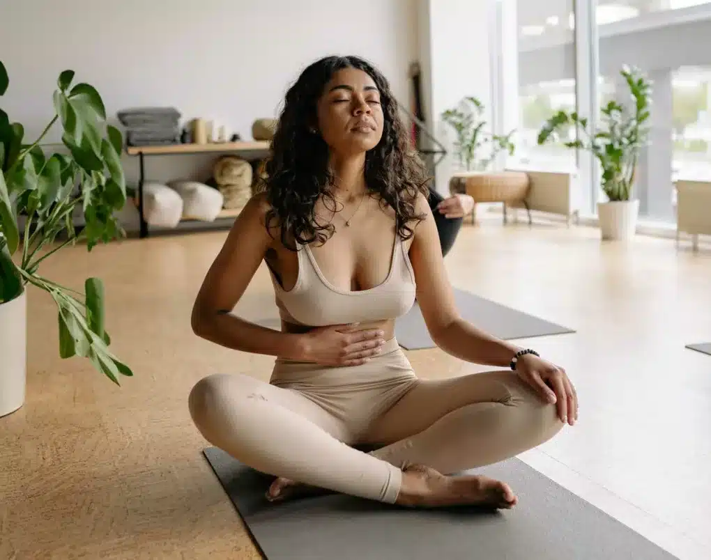 Frau sitzt auf einer Yogamatte, hält sich den Bauch und macht die Bauchatmung