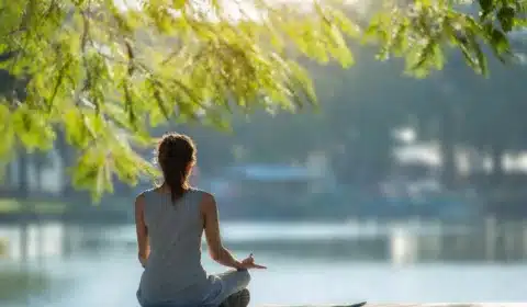 Frau sitzt am See und praktiziert Yoga und Meditation