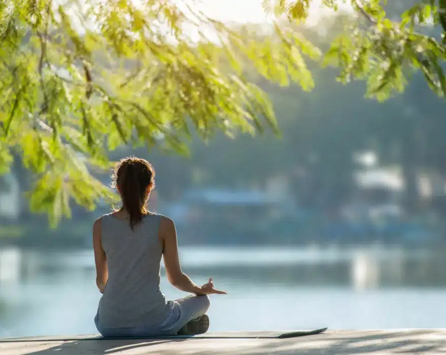Frau sitzt am See und praktiziert Yoga und Meditation