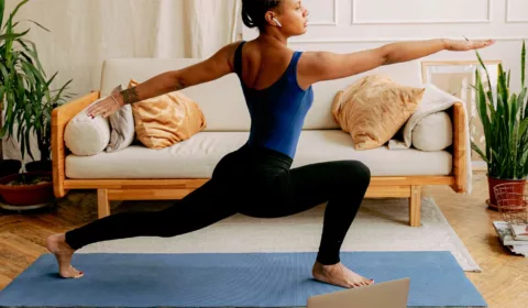 Frau macht zuhause vür dem Laptop Yoga im Wohnzimmer