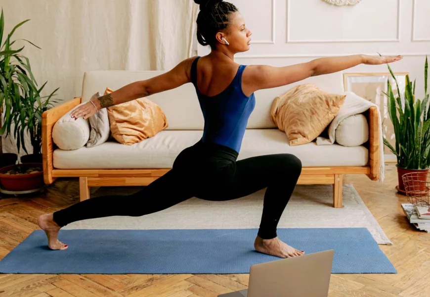 Frau macht zuhause vür dem Laptop Yoga im Wohnzimmer