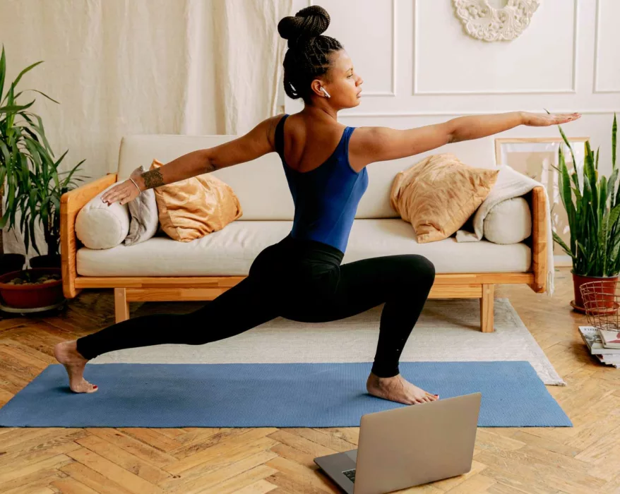 Frau macht zuhause vür dem Laptop Yoga im Wohnzimmer