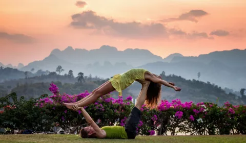 Mann und Frau beim Paar-Yoga mit Blumen im Hintergrund