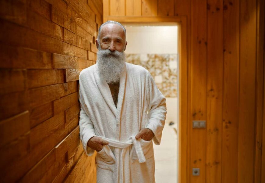 Lächelnder bärtiger Mann im Bademantel in der Sauna