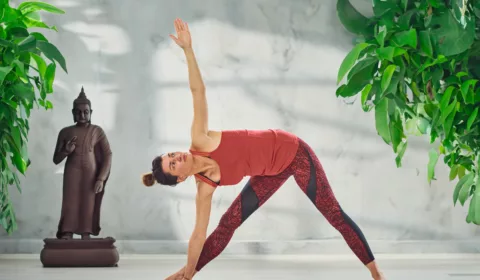 Attraktive Brünette in roter Sportkleidung, die barfuß eine Yoga-Dreieckshaltung einnimmt.