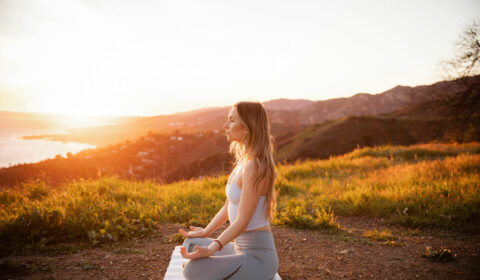 Seitenansicht einer meditierenden Sportlerin, die auf einer Übungsmatte sitzt, während die Sonne untergeht