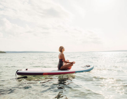 Frau meditiert auf ihrem SUP Board auf dem Wasser