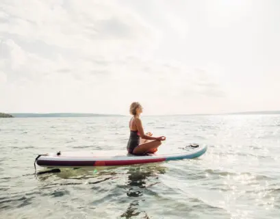 Frau meditiert auf ihrem SUP Board auf dem Wasser