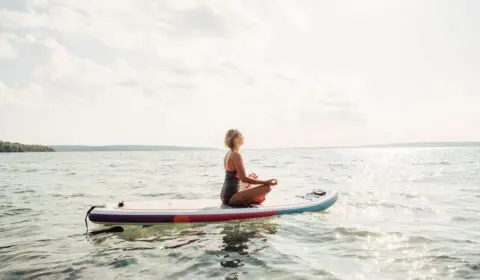 Frau meditiert auf ihrem SUP Board auf dem Wasser