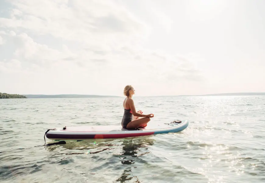 Frau meditiert auf ihrem SUP Board auf dem Wasser