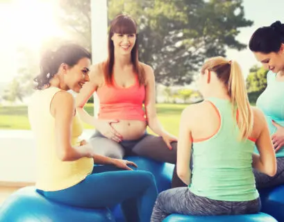 Glückliche schwangere Frauen sitzen auf Bällen im Yoga Urlaub