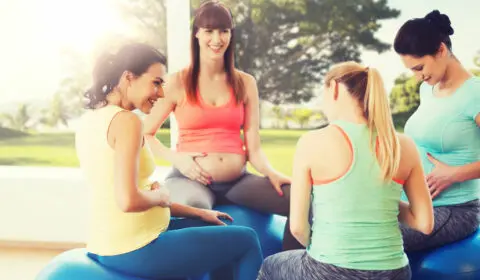 Glückliche schwangere Frauen sitzen auf Bällen im Yoga Urlaub