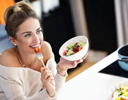 Schöne lächelnde Frau isst frischen vegetarischen Bio-Salat in der modernen Küche