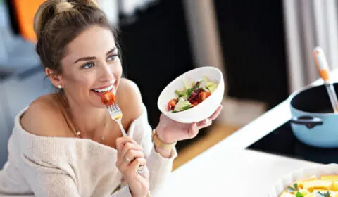 Schöne lächelnde Frau isst frischen vegetarischen Bio-Salat in der modernen Küche