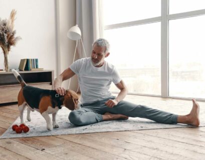 Glücklicher älterer Mann in Yogakleidung beim Training zu Hause in der Nähe seines Hundes