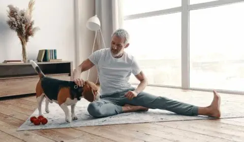 Glücklicher älterer Mann in Yogakleidung beim Training zu Hause in der Nähe seines Hundes