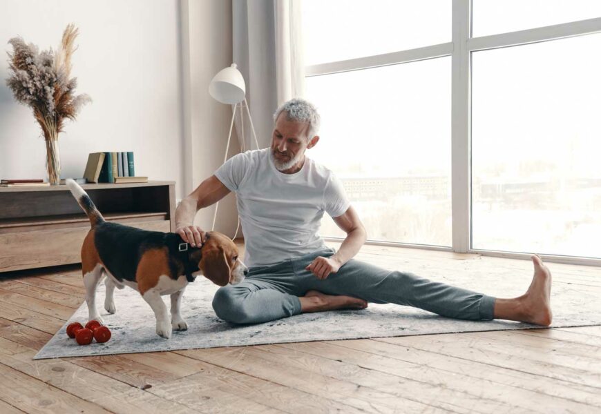 Glücklicher älterer Mann in Yogakleidung beim Training zu Hause in der Nähe seines Hundes
