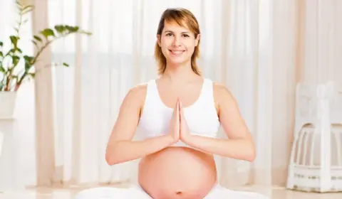 Schwangere Frau macht Yoga und schaut in die Kamera