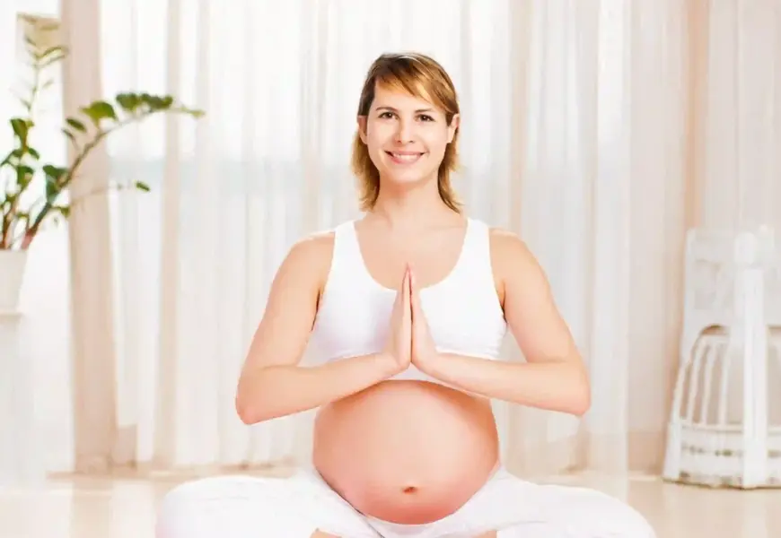 Schwangere Frau macht Yoga und schaut in die Kamera