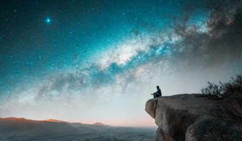 Mann sitzt auf einem Berg und meditiert unter dem nächtlichen Sternenhimmel