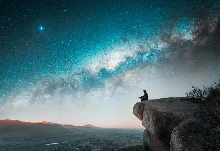 Mann sitzt auf einem Berg und meditiert unter dem nächtlichen Sternenhimmel