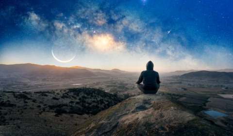 Mann sitzt auf einem Felsen in der Nacht und meditiert