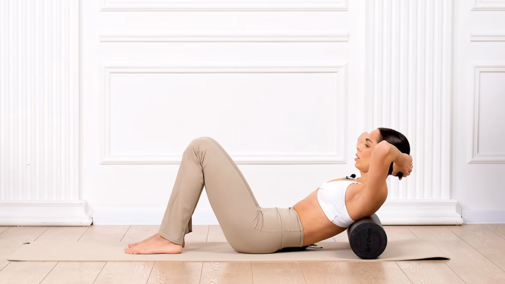 Frau macht Übungen auf der Yogamatte mit der Faszienrolle