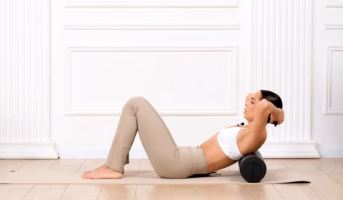 Frau macht Übungen auf der Yogamatte mit der Faszienrolle