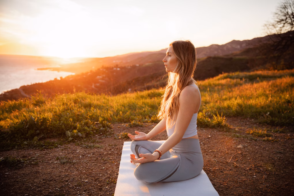 Frau sitzt am Meer und macht eine heilende Meditation