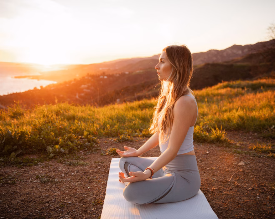 Frau sitzt am Meer und macht eine heilende Meditation