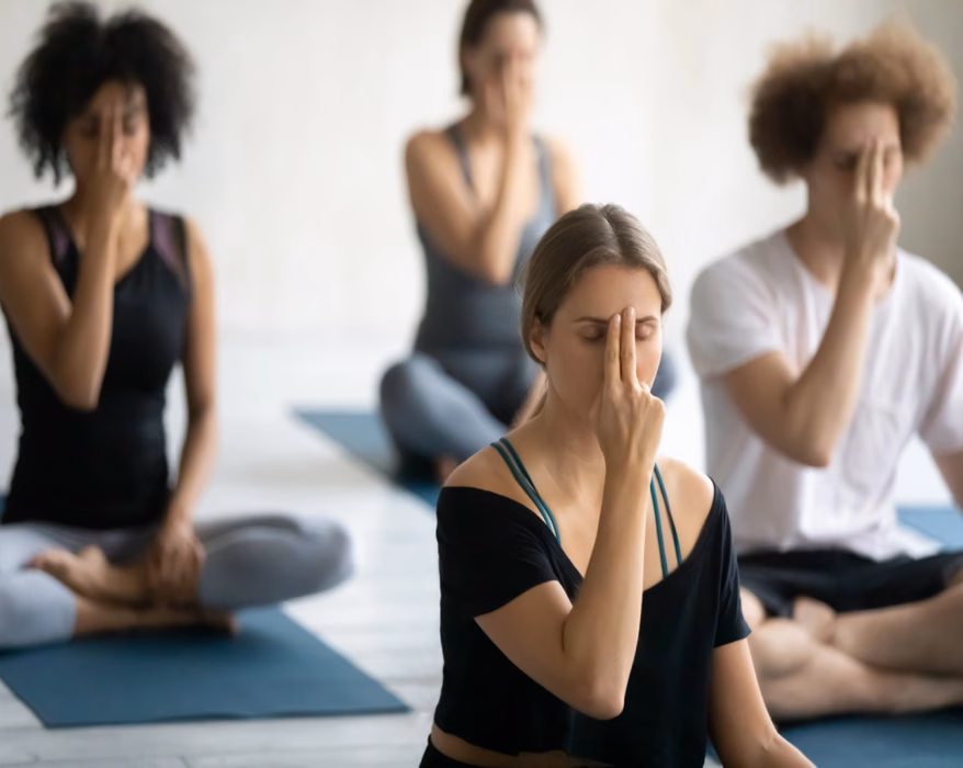 Vier Personen machen eine Meditation und halten sich mit zwei Finger das dritte Auge