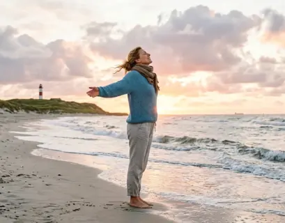 Entpannte Frau am Strand bei Sonnenaufgang, die tief einatmet und die Heilkraft der Klimatherapie genießt.