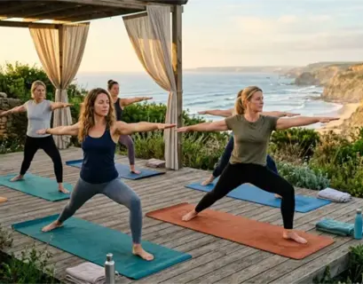 Eine Gruppe von Frauen praktiziert die Krieger-Yoga-Pose auf einer Holzterrasse an der Steilküste von Portugal bei Sonnenuntergang.